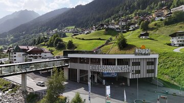 A modern building with the inscription "Kappl" in a mountainous landscape. In the background, green hills and small houses can be seen.