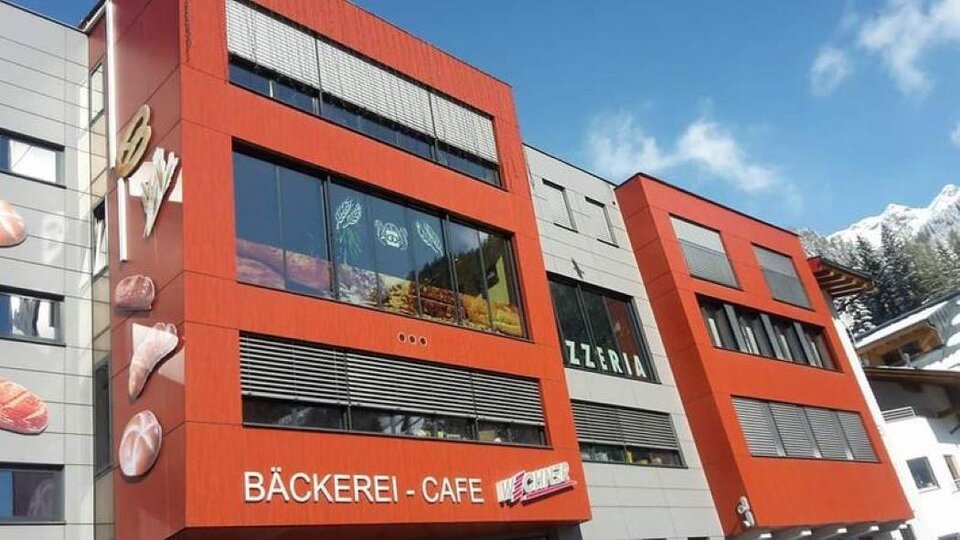 A modern building with a red facade and large windows. Inside, there is a bakery café and a pizzeria.