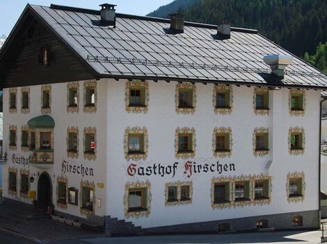 A traditional inn with the sign "Gasthof Hirschen" on the facade. The building has historical architecture and is located in a picturesque mountain landscape.